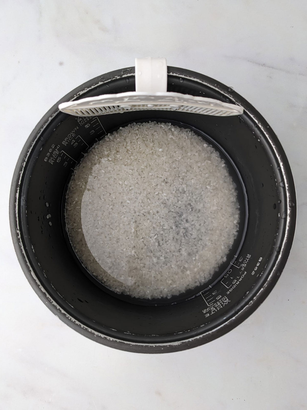 Washing the rice in a bowl with a rice strainer clip attached, on a white background.