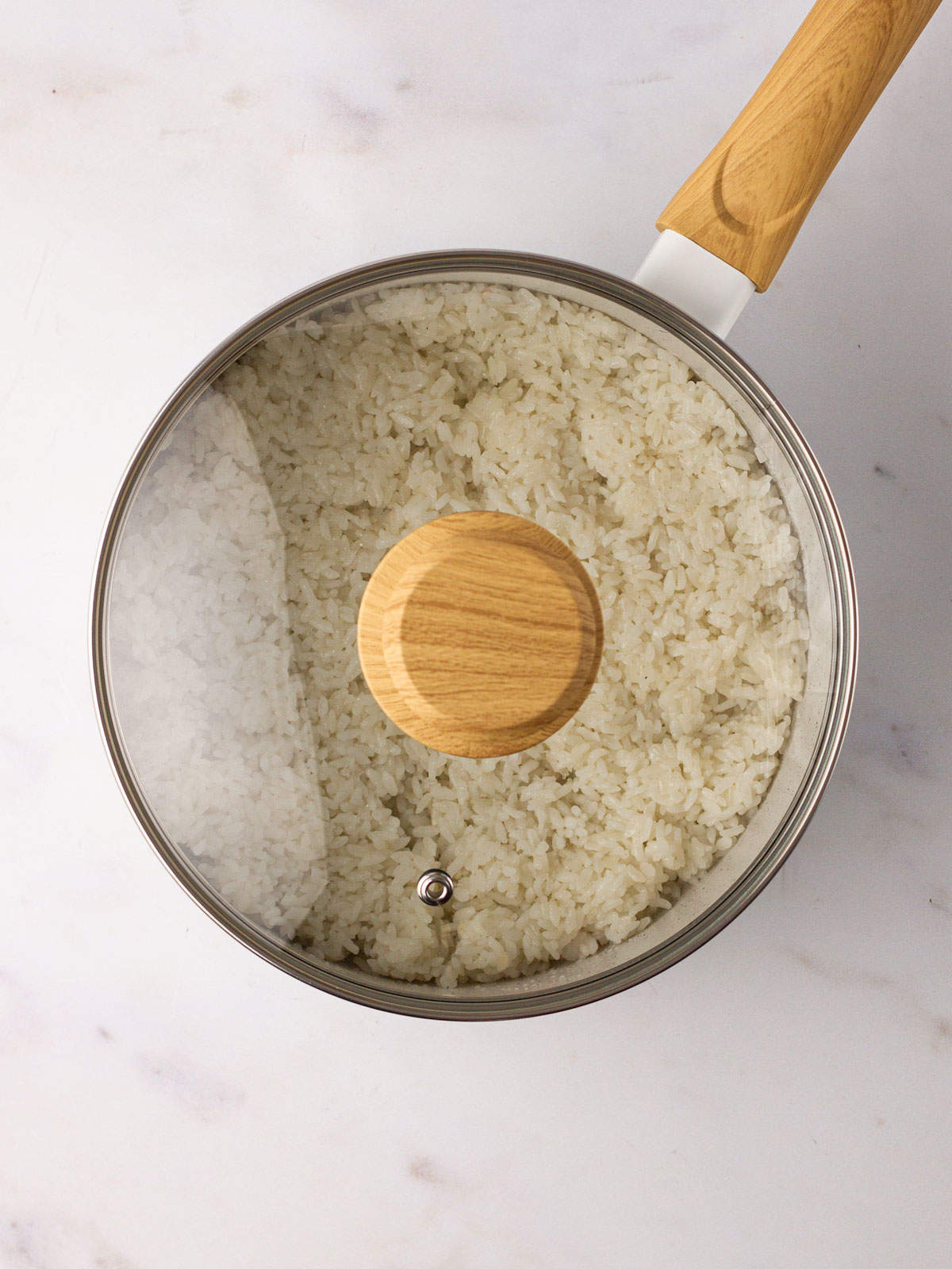 A heavy-bottomed saucepan on a white background containing the cooked rice which is resting with the lid on for 10 minutes.