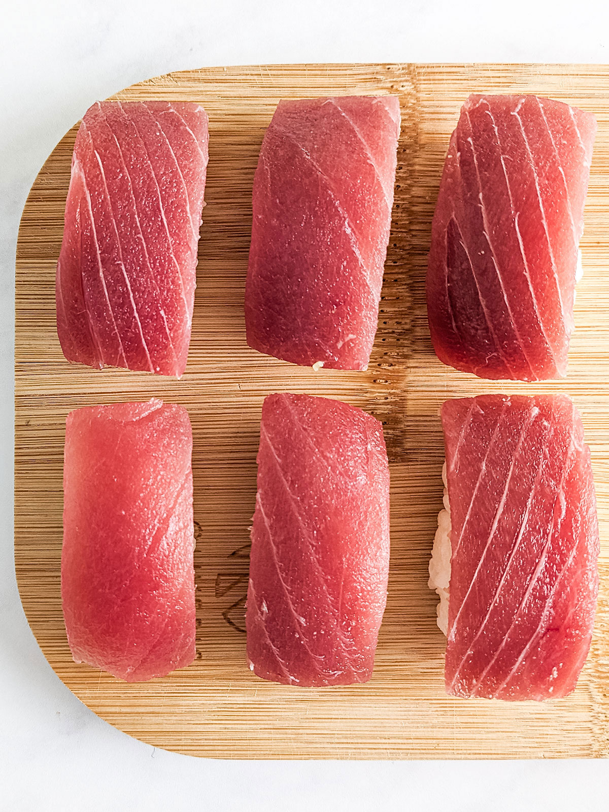 Six finished nigiri on a wooden board.