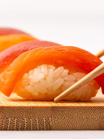 Close up of nigiri on a wooden board with chopsticks.