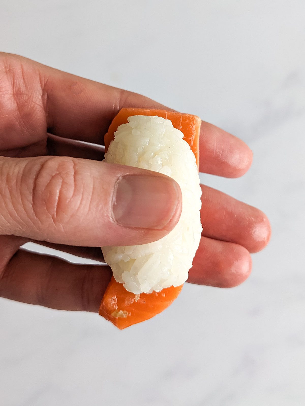 The shaped rice placed onto the slice of salmon with gentle pressure being applied to hold the fish in place.