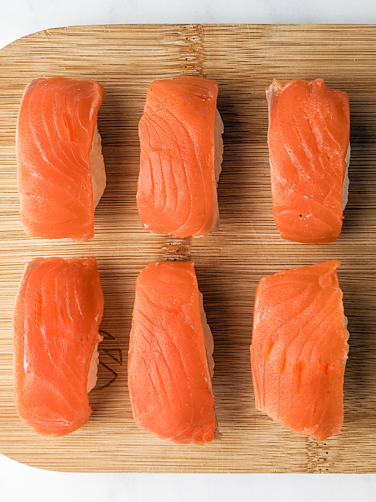 Six completed salmon nigiri on a wooden board.