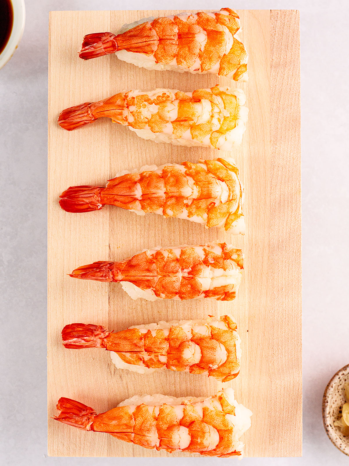 Six finished shrimp nigiri on a wooden board on a white background.