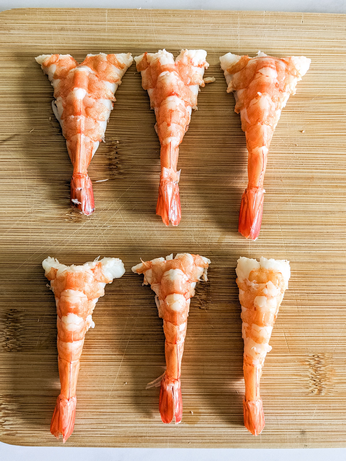 The butterflied shrimp lying flat on a wooden board.