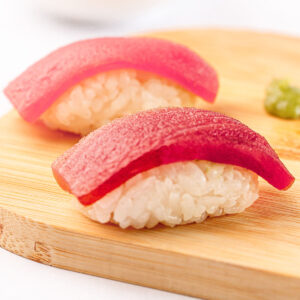 Two pieces of tuna nigiri on a wooden board with wasabi on the side.