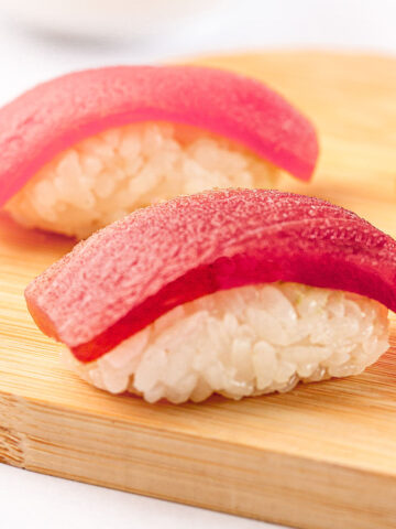 Two pieces of tuna nigiri on a wooden board with wasabi on the side.