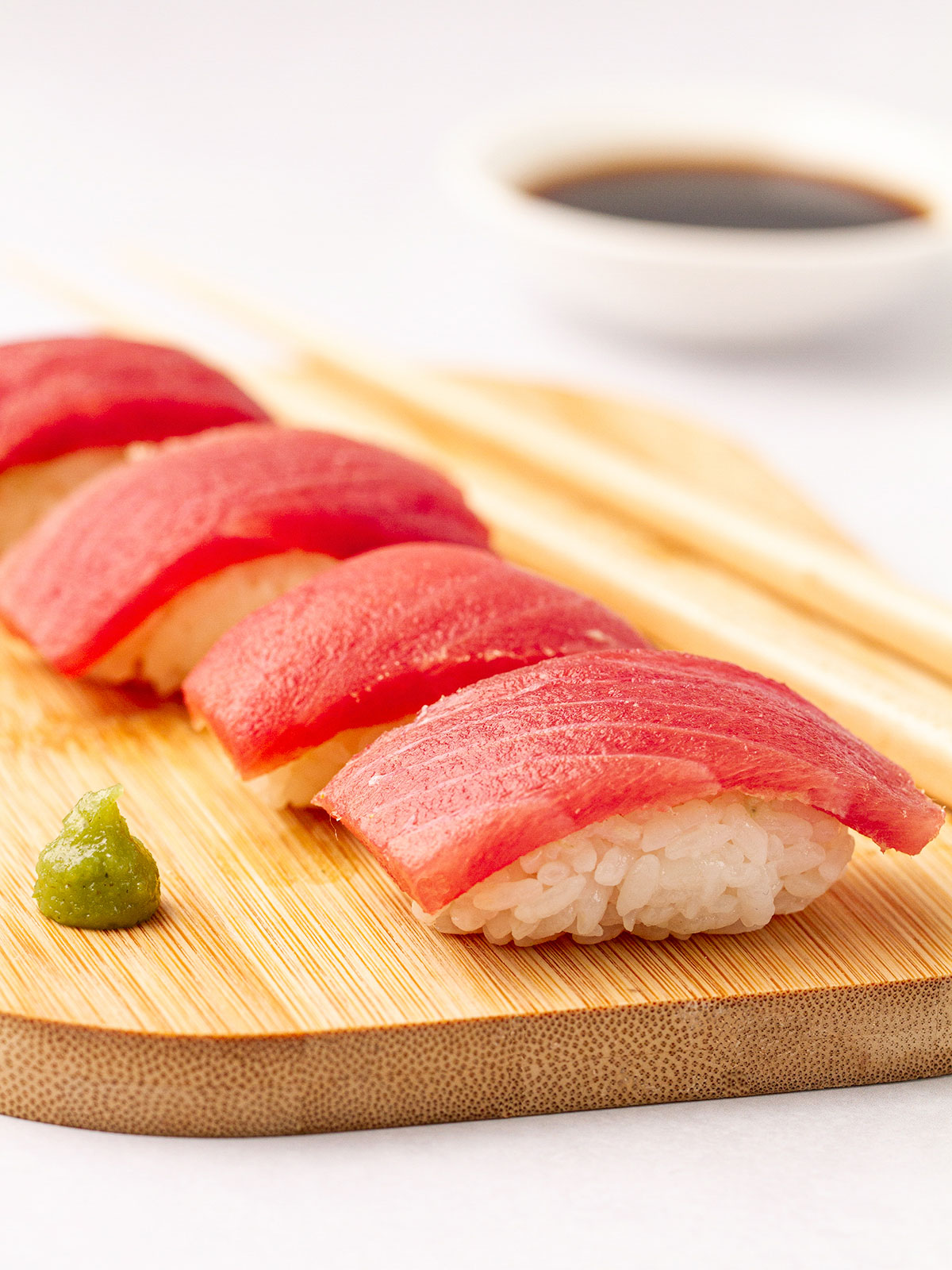 Close up of Tuna nigiri on a wooden board with wasabi on the side.