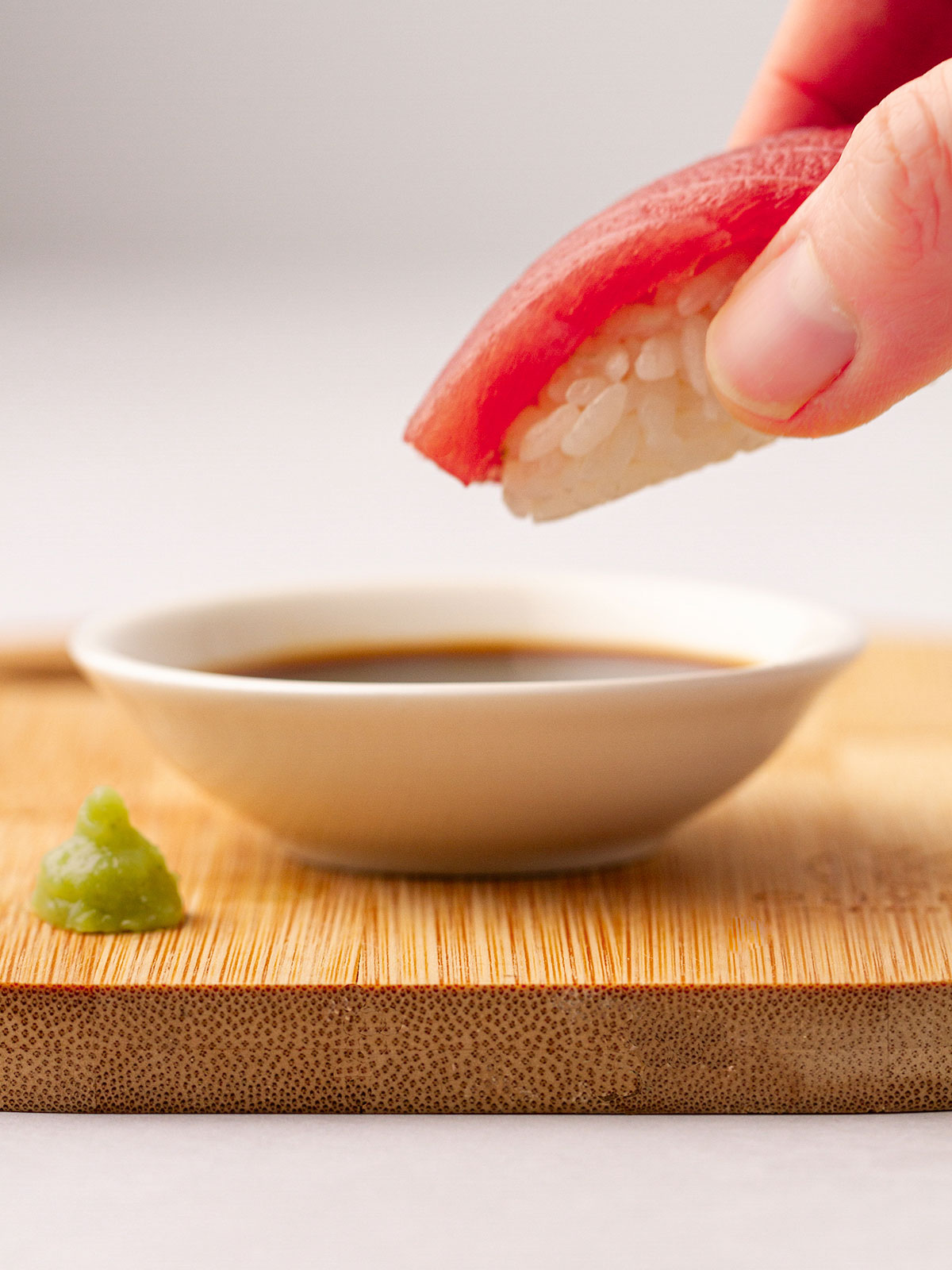 A nigiri in a hand about to be dipped into soy sauce.