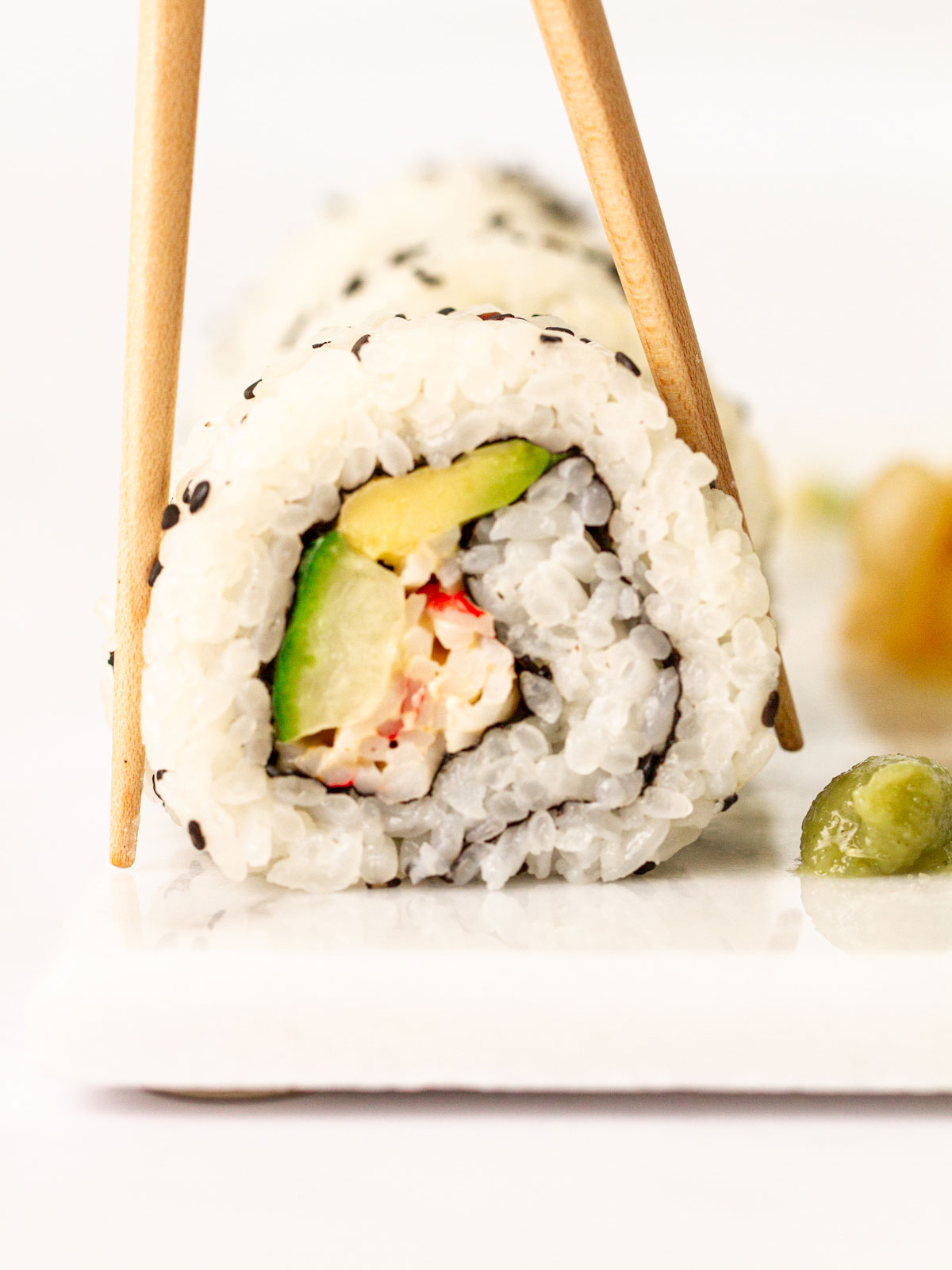 Close up of a Kani spicy crab roll with chopsticks and wasabi on a white board.