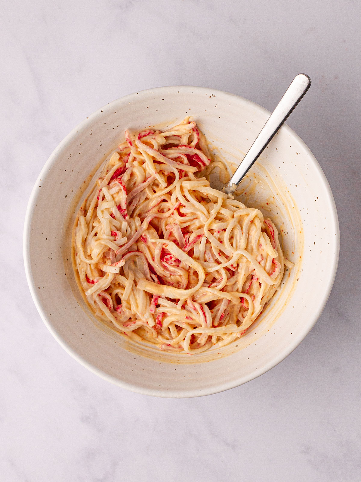 The mixture of mayo, rice vinegar, sugar, sriracha and crab meat in a white bowl on a white background