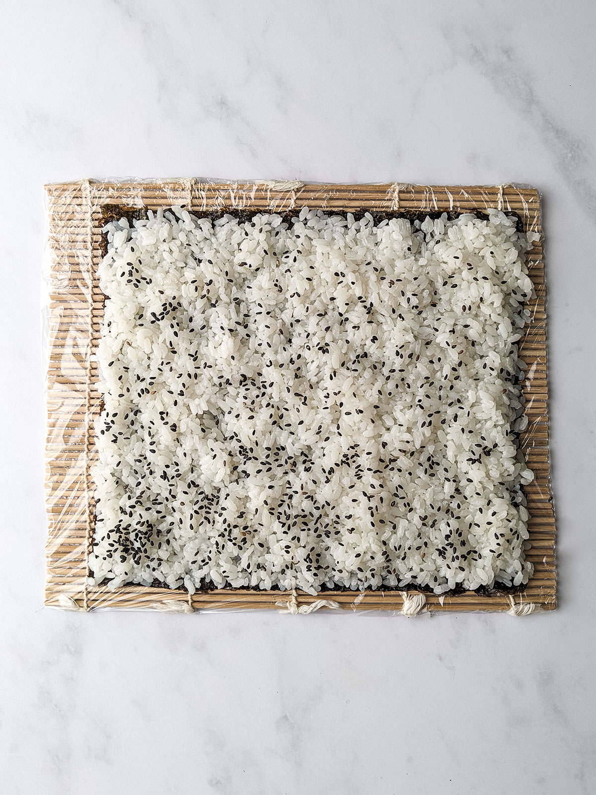 A large handful of rice spread evenly on the nori sheet leaving a ½ inch round the sides and sprinkled with sesame seeds.