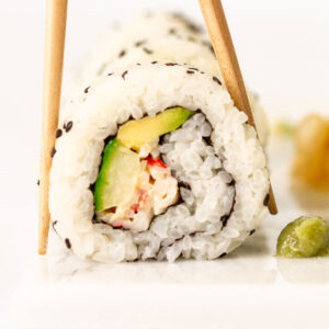 Close up of a Kani spicy crab roll with chopsticks and wasabi on a white board.