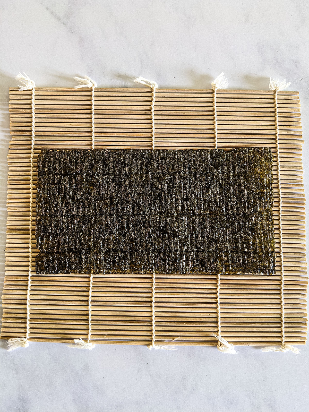 A halved nori sheet on the bamboo rolling mat with the rough side facing up, ready for the rice.