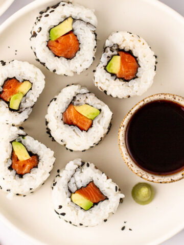 Salmon rolls on a plate with soy sauce.